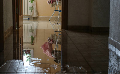 water flooding on floor in hallway with reflections visible showing damaged interior and laundry drying rack 3 water damage prevention tips