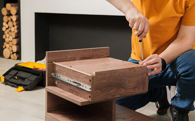 person assembling a wooden drawer with a screwdriver in a living room focused on DIY furniture projects