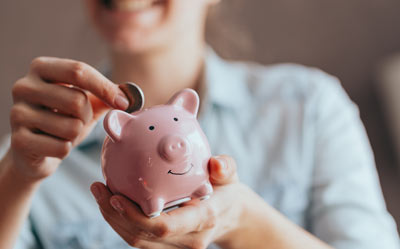 person smiling while inserting coin into pink piggy bank promoting 3 savings tips for financial growth