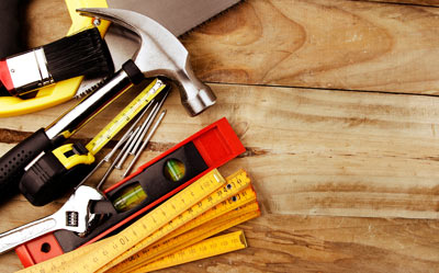 various hand tools on wooden surface with focus on hammer tape measure level and saw useful for five essential DIY projects