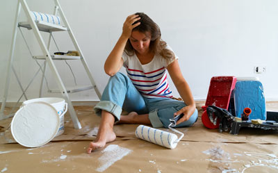 woman sitting on floor looking stressed surrounded by painting supplies and tools emphasizing a challenging renovation project