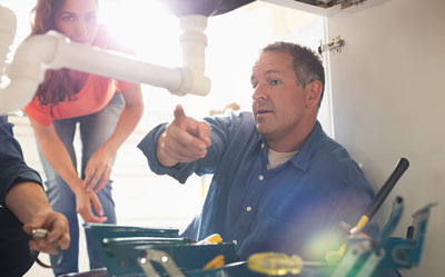 man explaining plumbing under sink with tools nearby including eight essential tools and woman observing