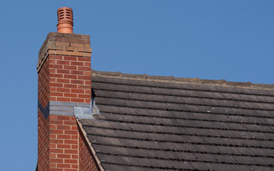 chimney on a brick house roof against a clear blue sky showing two sections of the roof tiles